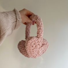 a hand holding a pink crocheted heart shaped object in front of a white wall