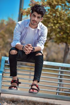 a man sitting on top of a metal bench next to a tree and wearing sandals