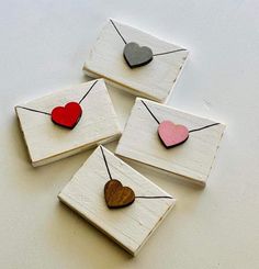 four small wooden hearts hanging from strings on white paper with black and red string attached to them