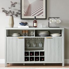 a white cabinet with wine glasses and plates on it in front of a framed photograph