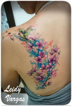 the back of a woman's shoulder with flowers and a bird tattoo on it