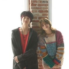 two people standing next to each other in front of a brick wall with sunlight coming through the window