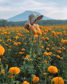 a person standing in a field of flowers with a hat on their head and one hand up