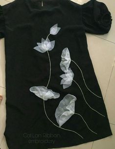 a black t - shirt with white flowers on it sitting on top of a tile floor