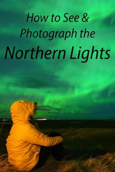 a person sitting on the ground looking at the sky with green lights in the background