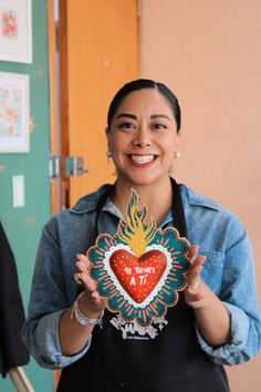 a woman is holding up a heart shaped object in her hands and smiling at the camera