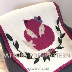 a knitted blanket with a fox and flowers on the front, sitting on a chair