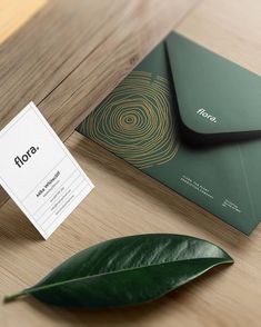 a close up of a business card on a table with a green leaf next to it