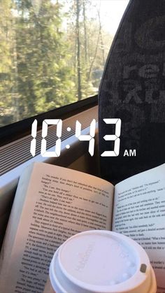 an open book sitting on top of a window sill next to a coffee cup