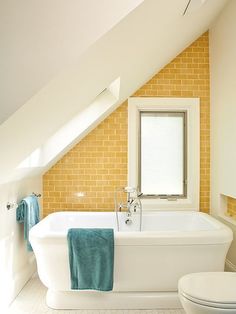 a white bath tub sitting next to a toilet in a bathroom under a slanted ceiling