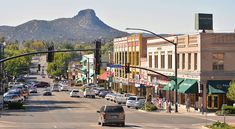 cars are driving down the street in front of buildings with mountains in the back ground