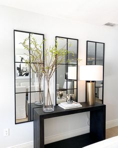 a black table topped with a vase filled with flowers next to two mirror wall mounted mirrors