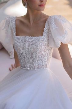 a woman in a white wedding dress sitting on a bed with her hands behind her back