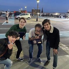 four people posing for a photo in the middle of a parking lot at night time