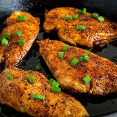 four pieces of chicken cooking in a skillet with scallions and green onions