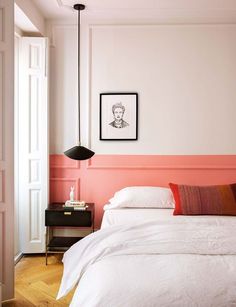 a bedroom with pink walls and white bedding, black lamp, framed portrait on the wall