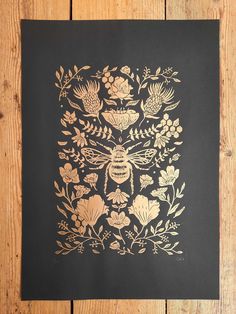 a black and gold paper with flowers and a bee in it on a wooden surface