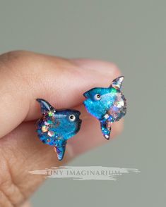 These mola mola or ocean sunfish stud earrings are the perfect gift for divers and ocean lovers. They are super adorable and derpy. These are ready made earrings and are available in blue or purplish pink. A great addition to your ocean jewelry collection! Each tiny mola mola earring measures approximately 1.3 cm (height) from fin to fin. Light weight and very comfortable to wear. These mola mola are made with resin and has some glitter details. The base is chameleon pigment and the color may ap Handmade Fish-shaped Earrings For Gifts, Blue Fish-shaped Earrings For Gift, Handmade Fish-shaped Jewelry Gift, Handmade Sterling Silver Fish-shaped Jewelry, Handmade Sterling Silver Fish Jewelry, Ocean-inspired Drop Earrings As Gift, Ocean Sunfish, Mola Mola, Jewelry Ocean