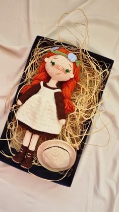 a crocheted doll sitting on top of a black box filled with hay and straw