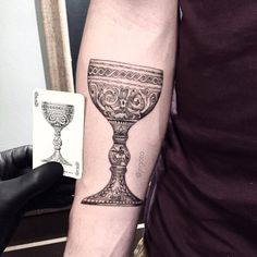 a man with a tattoo on his arm holding a playing card and a wine goblet