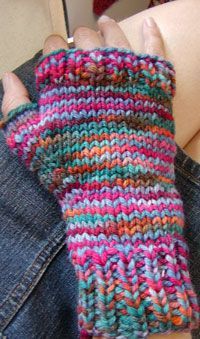 a woman's hand wearing a multicolored knitted mitt on her left arm