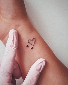 a person wearing gloves and holding their hand up to the wrist with a heart tattoo on it