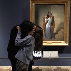 a man and woman kissing in front of a large painting on display at a museum