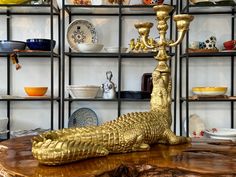 a gold alligator figurine sitting on top of a wooden table in front of shelves