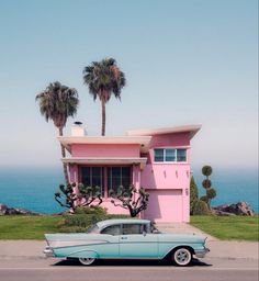 an old car parked in front of a pink house with palm trees on the beach