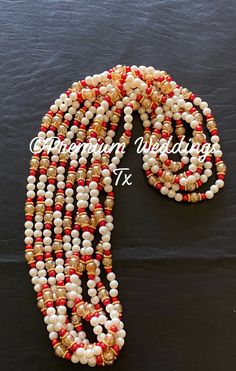 a necklace with red, white and gold beads is displayed on a black tablecloth