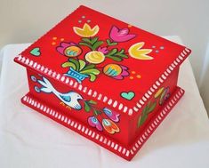 two red boxes with colorful designs on them sitting on a white tableclothed surface