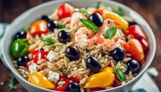 a white bowl filled with pasta salad and black olives, tomatoes, bell peppers, shrimp