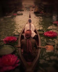 two people in a row boat on a body of water with pink flowers floating around