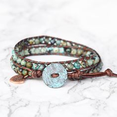 Genuine leather and African Turquoise stones make up this gorgeous double wrap bracelet. Always a favorite of jewelry addicts and fashionistas alike. If you want color, start here first. Features a beautiful rustic copper, Greek made button closure. A Bluefish Classic! 4mm(.157") diameter African Turquoise gemstones Unique Greek made copper button with patina, about 16mm (5/8") in diameter Rust brown leather Signature Bluefish logo heart charm 34 - 39 cm/13.5 - 15.5" length 2 button loop adjustm Turquoise Wrap Bracelet, Logo Heart, Boho Wrap Bracelet, Double Wrap Bracelet, African Turquoise, Turquoise Stones, Boho Bracelets, Turquoise Gemstone, Leather Wraps