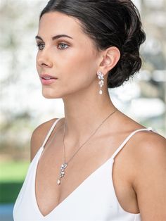 a woman in a white dress wearing a necklace and earring with flowers on it