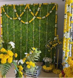 flowers and greenery are arranged in front of a green wall that is decorated with white and yellow flowers