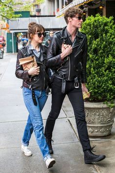 a man and woman walking down the street with their hands in each other's pockets