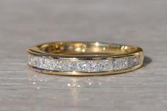 a yellow gold wedding band with princess cut diamonds on the inside and outside, sitting on a wooden surface