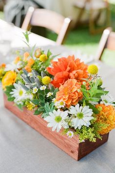 an arrangement of flowers in a wooden box on a table with white and orange flowers