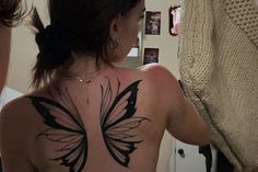 a woman with a butterfly tattoo on her back is looking at herself in the mirror