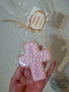 a hand holding a pink cookie shaped like a cross with a tag attached to it