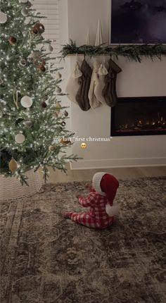 a christmas tree with stockings hanging from it's branches and a baby sitting on the floor