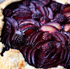 a close up of a pie with plums on it and crumbled crust