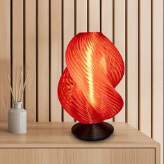 a red lamp sitting on top of a wooden table next to a vase and reeds