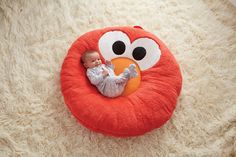 a baby laying on top of a round pillow with an orange ball in it's mouth