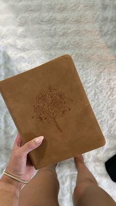 a woman is holding a brown book with flowers on it and her feet in the air