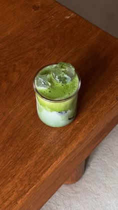 a small glass filled with green liquid on top of a wooden table