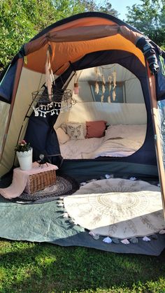 a tent is set up in the grass with pillows and blankets on it, next to a potted plant