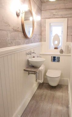 a white toilet sitting next to a sink in a bathroom under a round mirror on the wall