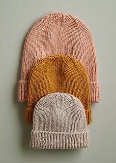 two knitted hats sitting next to each other on top of a gray surface,